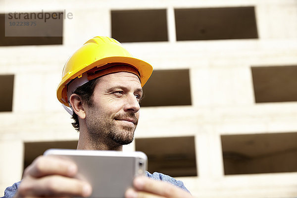 Mann mit Schutzhelm auf der Baustelle mit Mobiltelefon