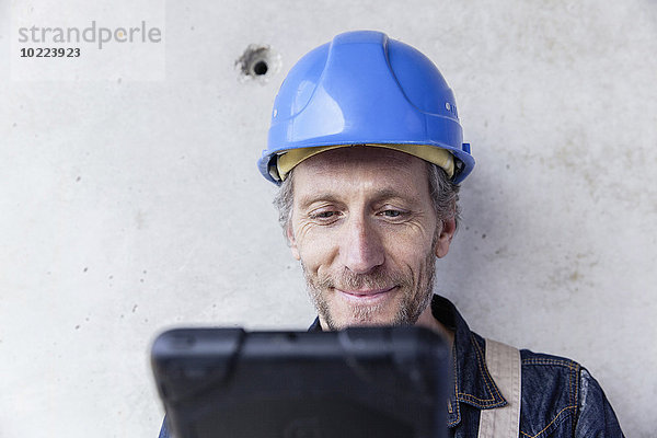 Lächelnder Mann mit Schutzhelm beim Betrachten des digitalen Tabletts