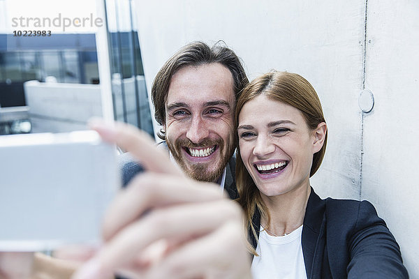 Porträt von zwei lachenden Geschäftsleuten  die einen Selfie mit Smartphone nehmen