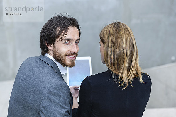 Zwei Geschäftsleute sitzen Seite an Seite mit digitalem Tablett