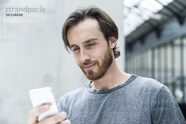 Porträt eines jungen Mannes mit Blick auf sein Smartphone