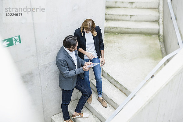 Zwei Geschäftsleute stehen auf einer Treppe und schauen auf ein digitales Tablett.