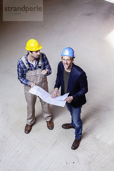 Bauarbeiter und Architekt mit Plangespräch auf der Baustelle