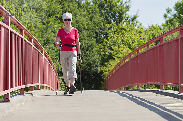 Seniorin beim Nordic Walking über eine Fußgängerbrücke