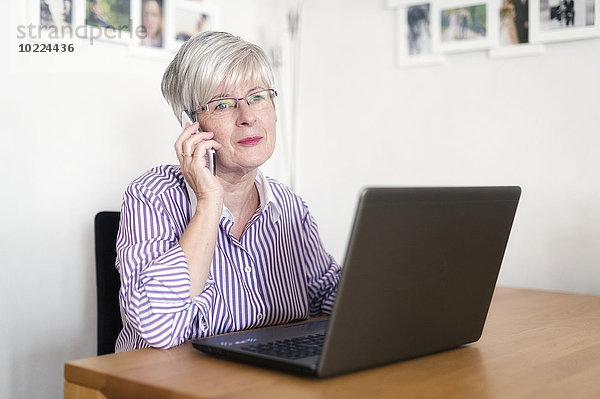 Portrait einer älteren Frau mit Laptop-Telefonie mit Smartphone