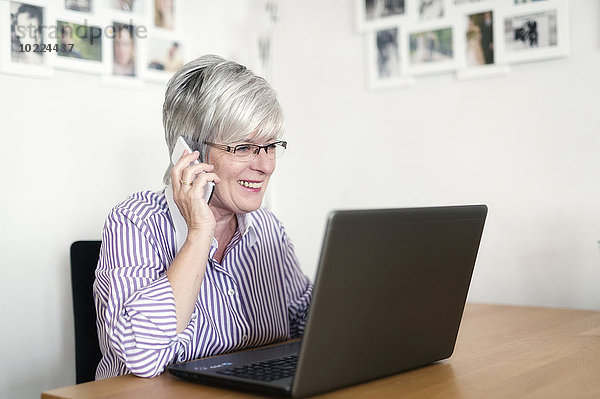 Portrait einer älteren Frau mit Laptop-Telefonie mit Smartphone
