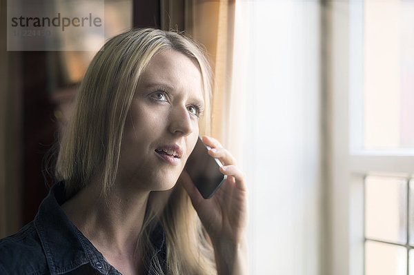 Portrait einer blonden Frau beim Telefonieren mit dem Smartphone
