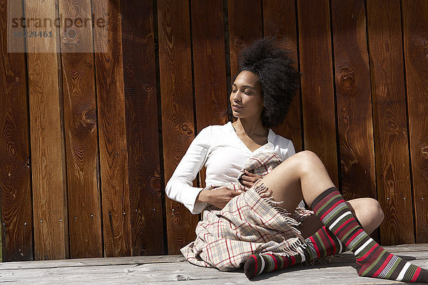 Sonnenbadende junge Frau auf Holzwand gelehnt