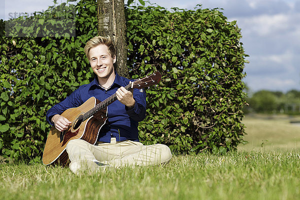 Lächelnder junger Mann spielt Gitarre auf der Wiese