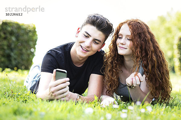 Teenager-Paar auf einer Wiese liegend mit Blick auf Smartphone