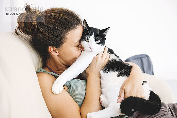 Frau sitzt auf dem Sofa und umarmt ihre Katze.