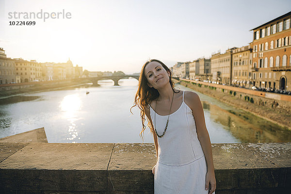 Italien  Florenz  Porträt einer Frau in weißem Sommerkleid  die bei Sonnenuntergang auf einer Brücke steht.
