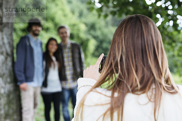 Junge Frau beim Fotografieren ihrer drei Freunde mit der Kamera