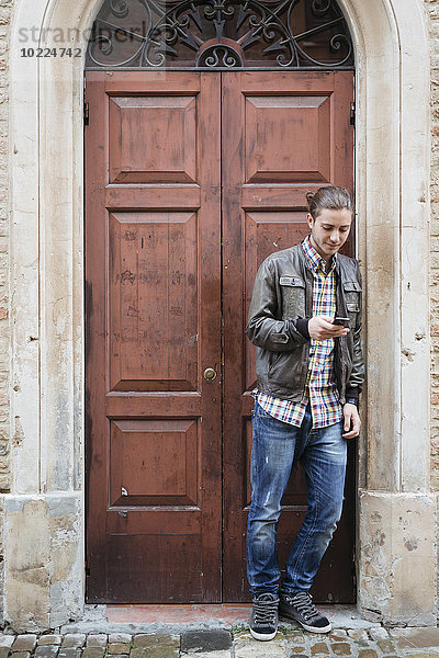 Italien  San Gimignano  junger Mann vor der Haustür mit seinem Smartphone