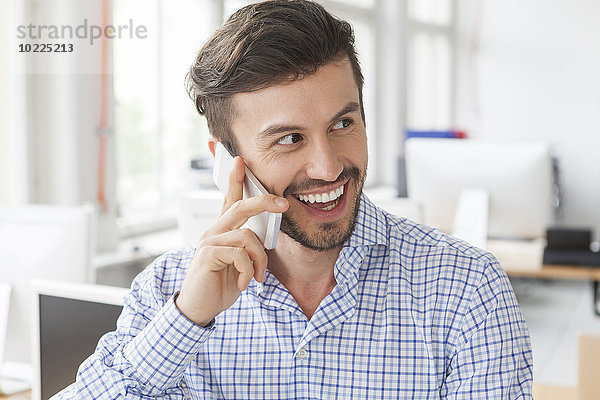Porträt eines lächelnden Geschäftsmannes beim Telefonieren im Büro