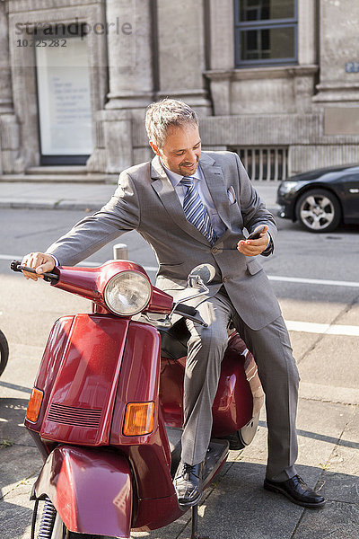 Deutschland  Stuttgart  lächelnder Geschäftsmann auf Motorroller sitzend