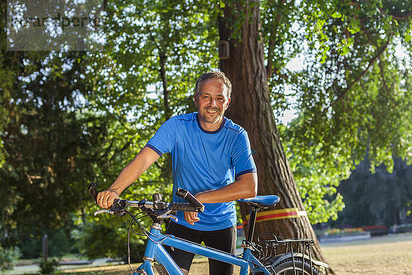 Porträt eines lächelnden Mannes im Park mit Fahrrad