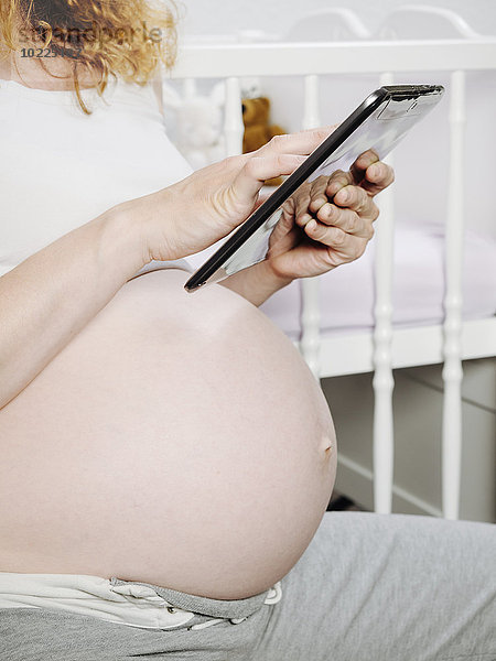 Schwangere vor dem Kinderbett mit einem digitalen Tablett