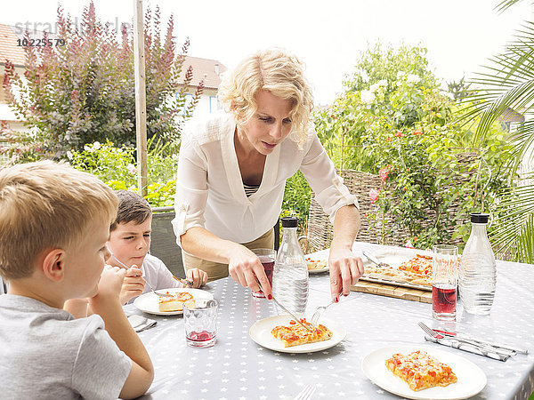 Mutter und ihre beiden Söhne essen zusammen Pizza auf der Terrasse.