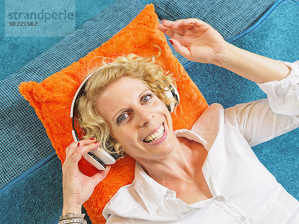 Porträt einer lächelnden blonden Frau beim Musikhören mit Kopfhörern
