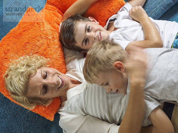 Mutter und ihre beiden Söhne entspannen sich gemeinsam auf dem Teppich zu Hause.
