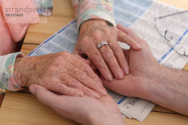 Hände einer älteren Frau  die die Hände eines Mannes hält.