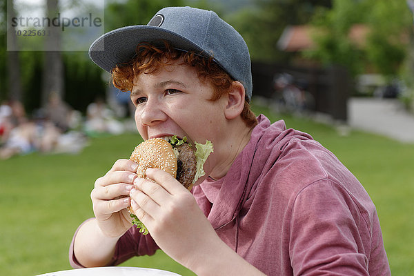 Teenager Junge mit Baseballkappe beim Hamburgeressen