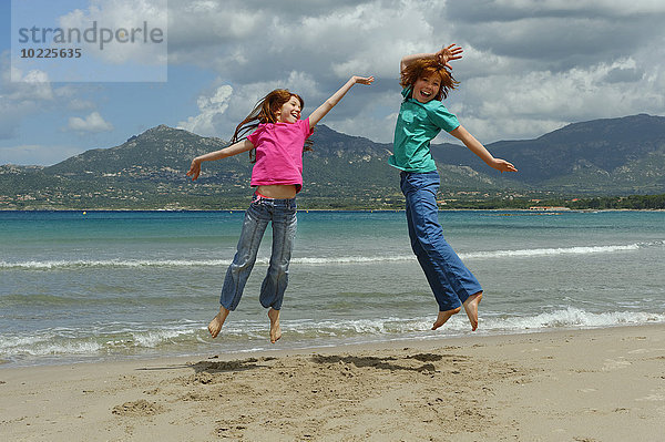 Frankreich  Korsika  Calvi  zwei Kinder  die am Strand in die Luft springen