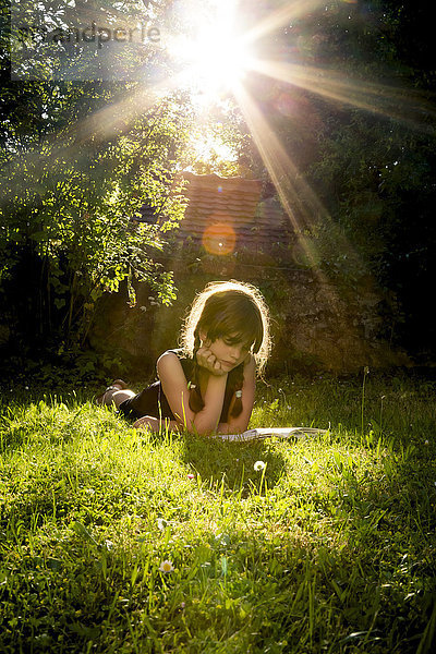 Mädchen liegt auf einer Wiese und liest ein Buch.