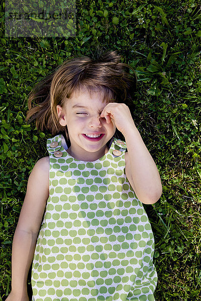 Lächelndes kleines Mädchen mit geschlossenen Augen auf einer Wiese liegend