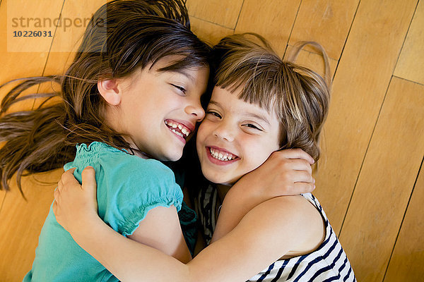 Zwei glückliche Schwestern  die sich auf dem Holzboden umarmen.