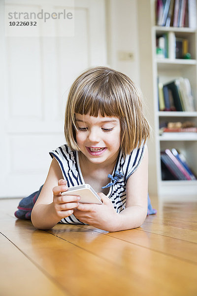 Porträt eines lächelnden Mädchens auf Holzboden liegend mit Smartphone