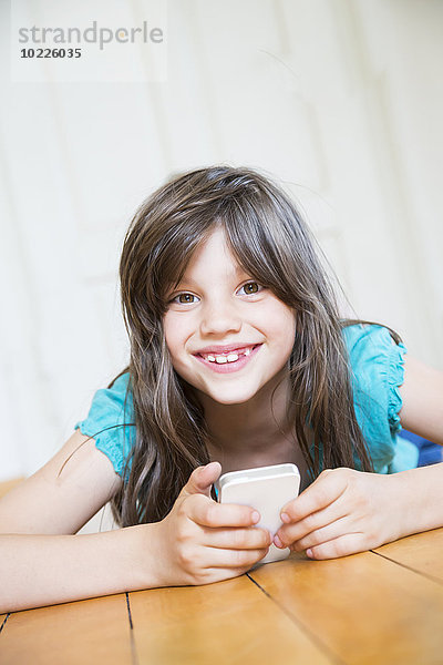 Porträt eines lächelnden Mädchens auf Holzboden mit Smartphone