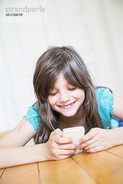 Lächelndes Mädchen auf Holzboden liegend mit Smartphone
