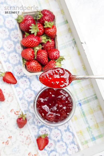 Löffel Erdbeermarmelade und Dose Erdbeeren im Hintergrund
