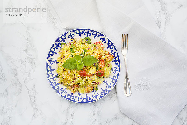 Teller mit Couscous-Salat  Tuch und Gabel auf weißem Marmor