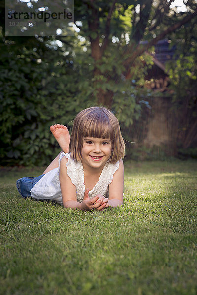 Lächelndes kleines Mädchen auf der Wiese im Garten liegend
