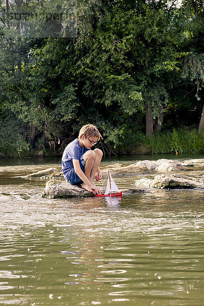 Junge spielt mit Holzspielzeugboot am Fluss