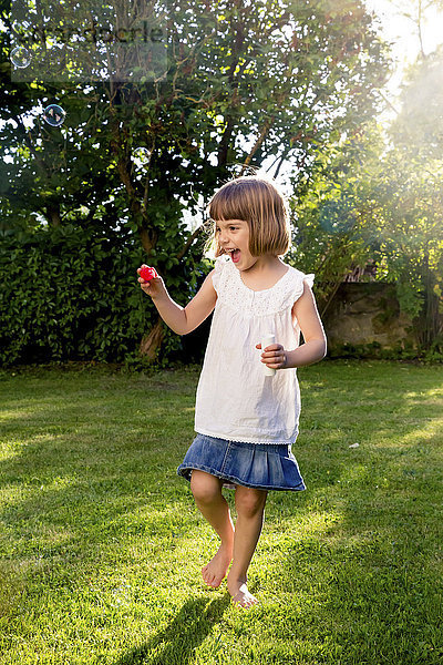 Kleines Mädchen spielt mit Seifenblasen im Garten