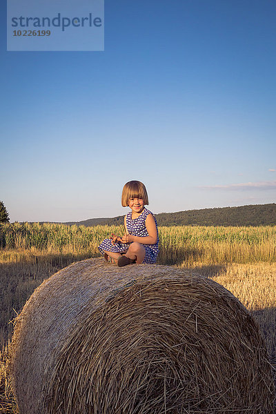Lächelndes kleines Mädchen auf Strohballen sitzend