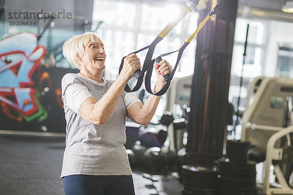 Glückliche Seniorin im Fitnessstudio beim Suspensionstraining