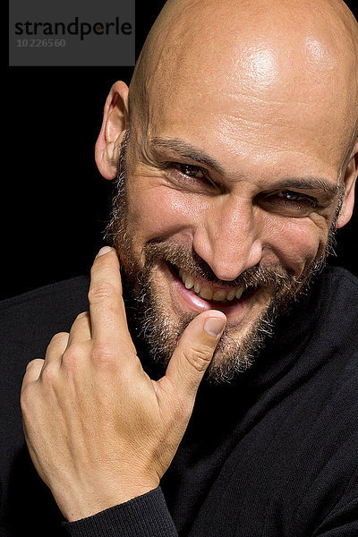 Porträt eines lächelnden Mannes mit Finger auf dem Mund vor schwarzem Hintergrund