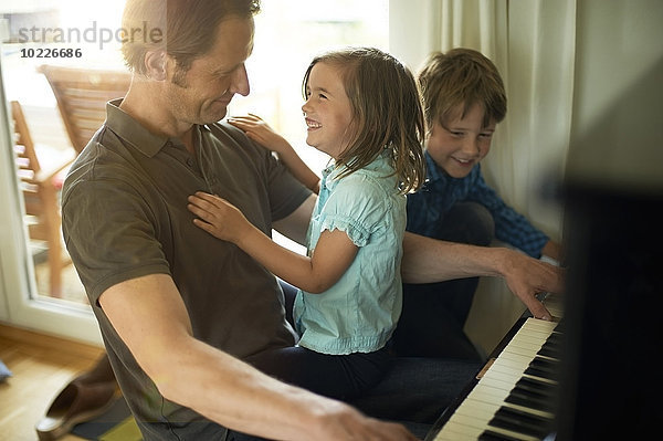 Vater spielt Klavier mit Tochter auf dem Schoß  Sohn schaut zu