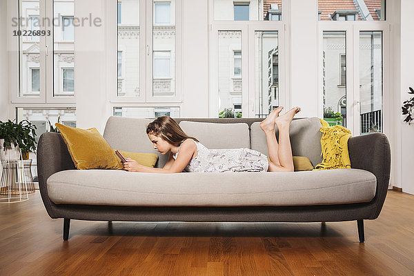 Kleines Mädchen beim Entspannen mit digitalem Tablett auf der Couch im Wohnzimmer