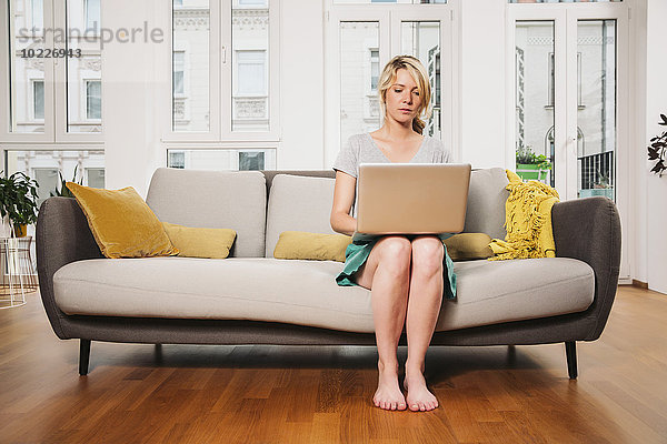Frau sitzend auf einer Couch im Wohnzimmer mit Laptop