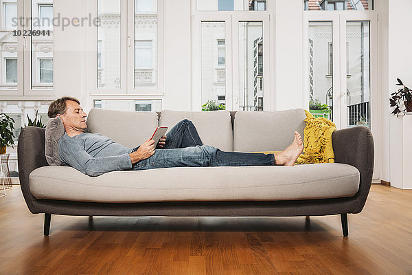 Mann entspannt mit digitalem Tablett auf der Couch im Wohnzimmer