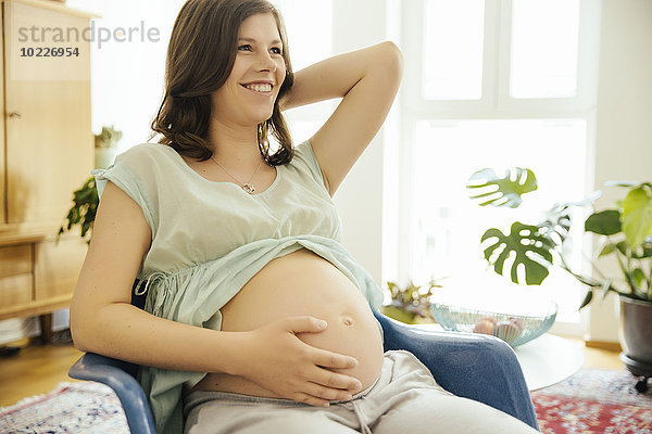 Glückliche schwangere Frau auf einem Stuhl zu Hause sitzend