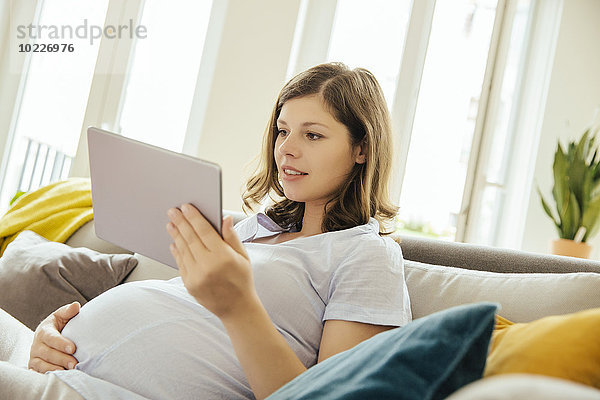 Schwangere mit digitalem Tablett zum Entspannen auf der Couch zu Hause