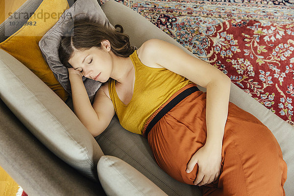 Eine schwangere Frau macht zu Hause ein Nickerchen auf ihrer Couch.