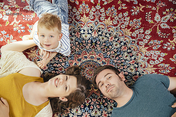 Gruppenbild von Eltern und kleinem Sohn auf einem Perserteppich zu Hause liegend